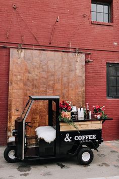 a coffee truck parked in front of a red brick building with flowers on the back