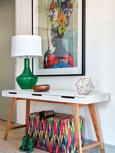 a white table topped with a green vase next to a lamp and a painting on the wall