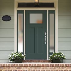 a green front door with two planters on the steps and a light above it