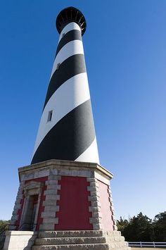 a large black and white lighthouse on top of a stone platform with steps leading up to it