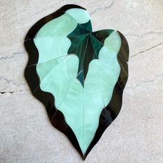 a green leaf shaped paper decoration on the floor in front of a marble wall with black and white designs