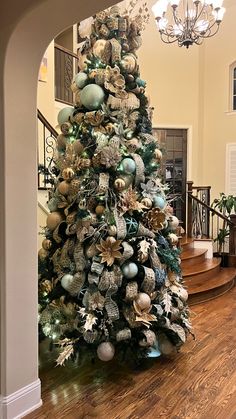 a decorated christmas tree in the middle of a room with stairs and chandelier