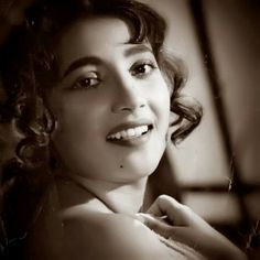 black and white photograph of a woman with curly hair smiling at the camera while wearing a dress