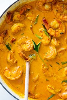 a pan filled with shrimp and sauce on top of a table next to a wooden spoon