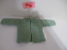 a green knitted sweater hanging on the wall next to a tag with an image of a fish