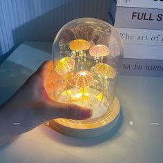 a hand is holding a glass dome with yellow flowers in it and some lights inside