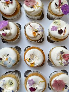 twelve cupcakes with white frosting and colorful flowers on them are arranged in a box