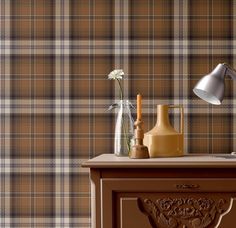 a table with a lamp, vase and other items on it in front of a plaid wallpaper