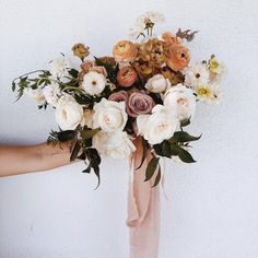 a woman holding a bouquet of flowers in her hand with white and peach colors on it