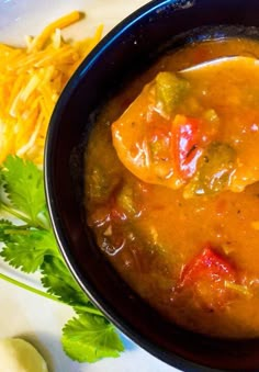 a black bowl filled with soup next to a pile of cheese and cilantro