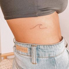 a woman's stomach with a small wave tattoo on the side of her belly