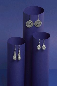 three pieces of jewelry sitting on top of a purple vase next to each other in front of a blue background