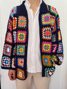 a man standing in front of a white door wearing a colorful crocheted jacket