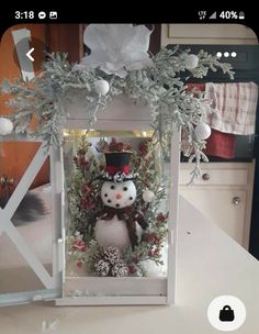 a snowman decoration in a white box on a counter with flowers and greenery