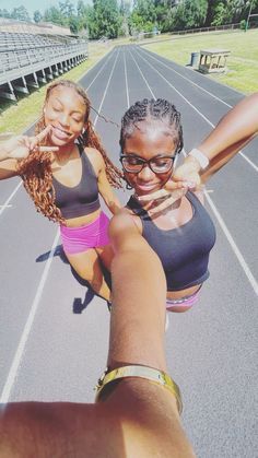 two young women taking a selfie on a track with their hands in the air