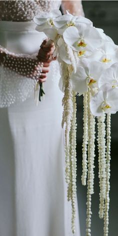 a woman in a white dress holding a bouquet of flowers with pearls on the stems