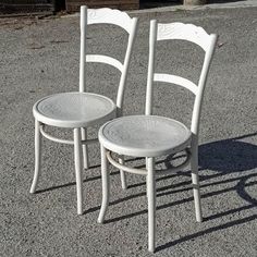 two white chairs sitting next to each other on top of a parking lot in front of a building