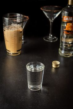 two shot glasses filled with liquid sitting on top of a table next to an empty bottle