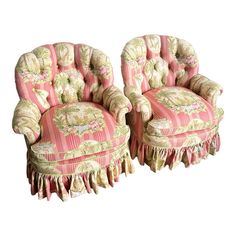 two pink chairs with floral designs and fringe trimmings on the back one chair has a matching footstool