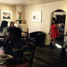 a woman sitting at a table with plates of food in front of her and two other women standing behind her