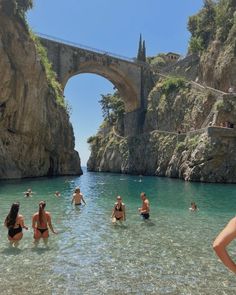 many people are swimming in the water near a stone bridge and an arch overpass