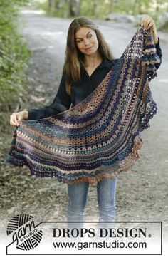 a woman holding up a crocheted shawl in front of her on the road