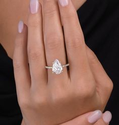 a woman's hand holding an engagement ring with a pear shaped diamond on it