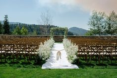 an outdoor ceremony setup with white flowers and greenery at the end of the aisle