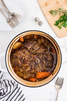 a pot filled with stew and carrots on top of a white counter next to silverware