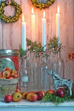 apples and other fruit are displayed in front of candles on a mantle with wreaths