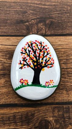 a painted rock on top of a wooden surface with a tree in the middle and leaves all over it