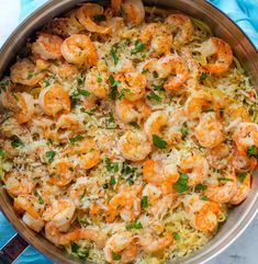 a pan filled with shrimp and rice on top of a blue table cloth next to a spoon