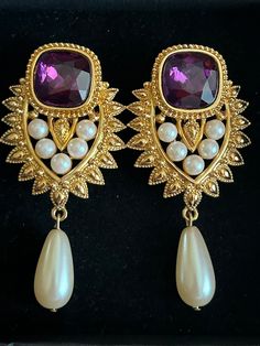 A beautiful pair of vintage runway clip on earrings by designer Shaill Jhaveri. These were designed for the Elizabeth Taylor Imperial Elegance Collection for Avon.  They are an elegant gold plated design with a glass purple emerald cut stone, with faux pearls in the middle. A large faux teardrop pearls dangles from the bottom  These are substantial and measure approximately 2 1/2 inches long, and 1 3/4 inches wide.  They are signed on the back: Jhaveri for Avon.  They are stunning, and in excell Glamorous Clip-on Earrings For Formal Events, Glamorous Clip-on Earrings For Formal Occasions, Glamorous Clip-on Earrings For Formal, Formal Costume Jewelry Clip-on Drop Earrings, Vintage Jeweled Clip-on Earrings For Evening, Vintage Clip-on Pearl Earrings For Gift, Vintage Pearl Clip-on Earrings For Gift, Luxury Vintage Clip-on Pearl Earrings, Vintage Evening Clip-on Crystal Earrings