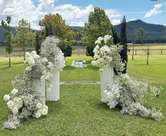 three white vases with flowers on them in the middle of a grassy area next to trees