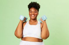 a woman holding two blue dumbs in front of her face and smiling at the camera