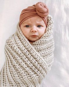 a baby wrapped up in a blanket and wearing a knitted headband with a knot on top