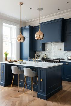 a kitchen with blue cabinets and marble counter tops, gold pendant lights over the island