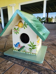 a birdhouse with a green roof on a tile floor in front of a yellow building