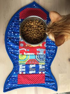 a cat eating food out of a bowl on top of a blue mat with red and white designs