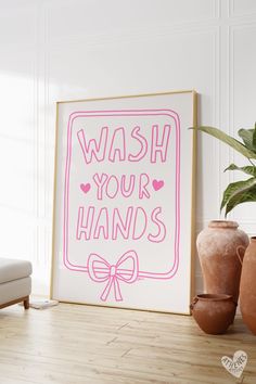 a pink wash your hands sign sitting next to two vases and a potted plant