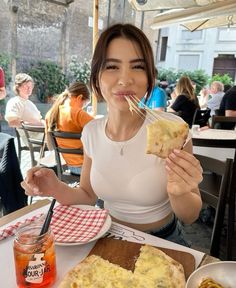 a woman sitting at a table with food in front of her and eating pizza on the other side