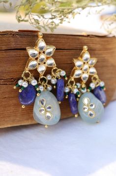 The Nessa kundan studs features beautiful myriad of kundan and blue stone drops. The versatile pair is replete with style and glamour. Closure - Push Back. There's a subtle yet clearly indisputable quality in our traditional attires that brings out the depth of a woman's femininity. The warm glory of the gold, the ritualistic richness of red and green, the clamor of payals and kadas, are a celebration of womanhood. The magic is in the gaze of the woman, her suave as she walks, shy of her own glo Blue Temple Jewelry Earrings With Latkans, Blue Fusion Earrings With Latkans, Blue Meenakari Earrings For Festive Season, Blue Bollywood Meenakari Earrings, Blue Festive Danglers, Blue Meenakari Earrings For Diwali, Blue Temple Jewelry Danglers For Diwali, Blue Meenakari Danglers For Celebration, Festive Blue Drop Earrings