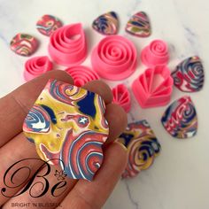 a person is holding some pink and blue swirls in their hand, next to small fondant shapes