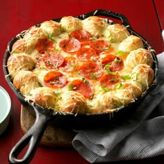 a pepperoni and cheese pizza in a cast iron skillet on a red table