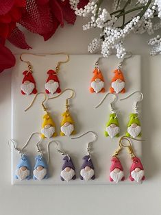 six pairs of colorful earrings on a white tray next to flowers and red flower petals