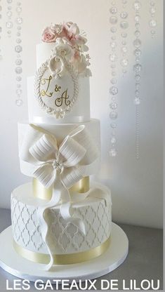 a three tiered white wedding cake with pink flowers and pearls on the top layer