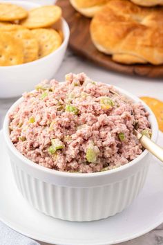 a white bowl filled with tuna salad on top of a plate next to crackers