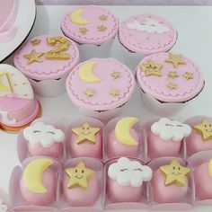 cupcakes decorated with stars, moon and clouds in pink frosting boxes on a table