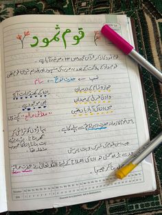 an open book with arabic writing and two pens