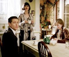 three people sitting at a table with cups in front of them and one person standing behind the table